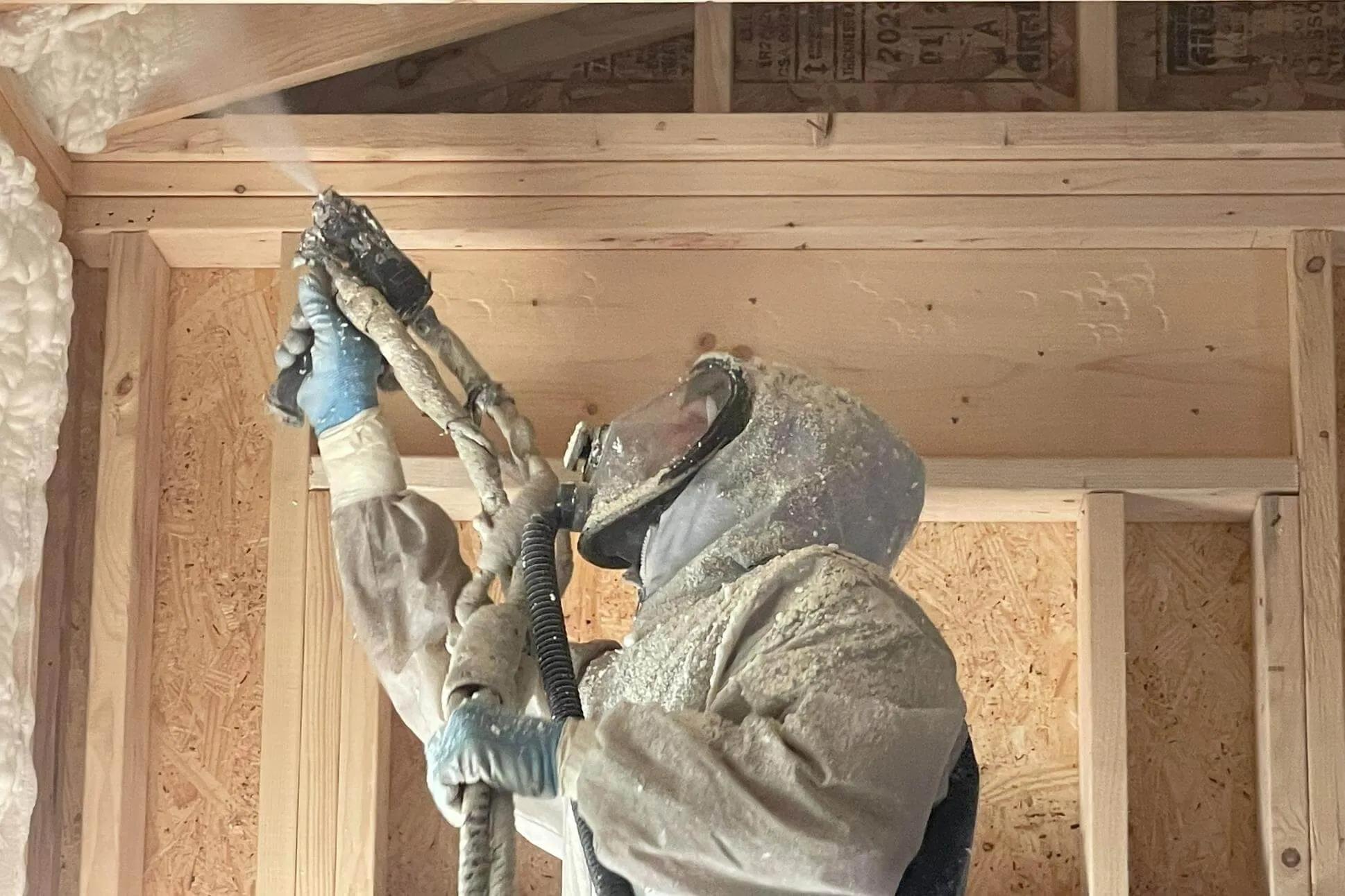 Installer spraying foam overhead in open framing