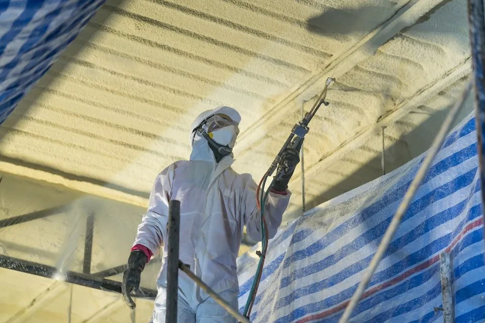 Installer spraying a roof deck with protective sheeting in place